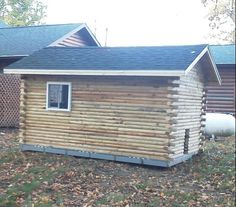 a small log cabin sitting in the grass next to a building with a black roof