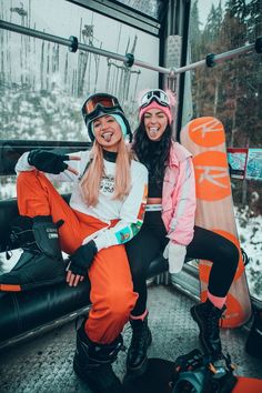 two snowboarders sitting on the back of a ski lift smiling at the camera