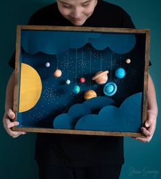 a man holding up a painting with planets in the sky and stars on it,