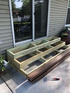 a wooden bench sitting in front of a window on top of a cement floor next to a potted plant