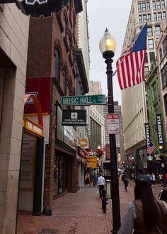 people walking down the street in front of buildings with american flags hanging from it's sides