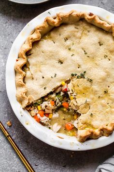 a chicken pot pie in a white dish with a slice missing from it and two forks next to it