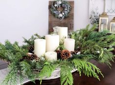 some candles are sitting on a table with pine cones and greenery