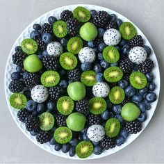 a white plate topped with sliced kiwis and blueberries next to blackberries