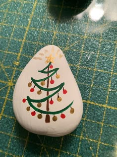 a painted rock with a christmas tree on it sitting on a green counter top next to a potted plant