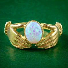 A fabulous Edwardian style ring depicting two hands presenting a colourful cultured opal cabochon, set in a milgrain bezel mount. The design is similar to an Irish Claddagh ring and is fashioned in silver with an 18ct yellow gold gilt finish.  Opal is the birthstone of October. Their magic has been revered throughout history, desired for their enchanting rainbow of colours that flow and dance across the surface of the stone, evoking the beauty of planet earth or the aurora borealis, with a burni Heirloom Style Cabochon Opal Ring For Formal Occasions, Heirloom Cabochon Opal Ring For Formal Occasions, Heirloom Style Opal Cabochon Ring For Formal Occasions, Heirloom Style Formal Opal Cabochon Ring, Victorian Cabochon Opal Ring For Gift, Victorian Style Cabochon Opal Ring Gift, Victorian Opal Cabochon Ring As Gift, Heirloom Bezel Set Opal Ring For Formal Occasions, Heirloom Style Bezel Set Opal Ring For Formal Occasions