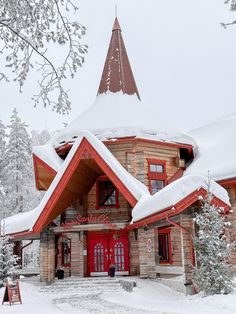 a red and brown building with snow on the ground around it's roof, surrounded by trees