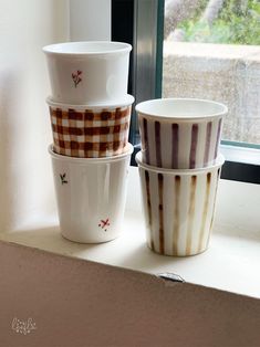 three cups sitting on top of a window sill