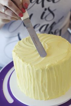 a woman cutting into a yellow cake with a knife on it's side and the frosting is white