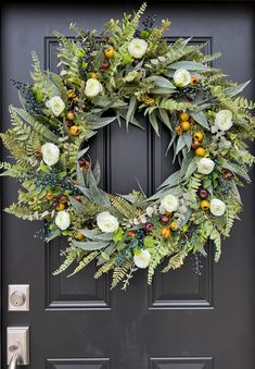 a wreath on the front door with white flowers and greenery hanging from it's sides