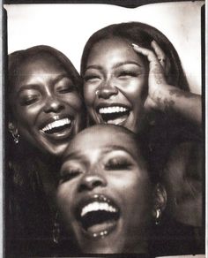 three women laughing together with their mouths open and one holding her head in the other's hands