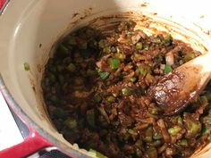 a pot filled with meat and vegetables on top of a stove next to a wooden spoon