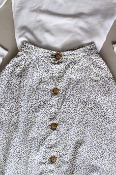 a skirt with buttons on the front and bottom, sitting next to a white shirt