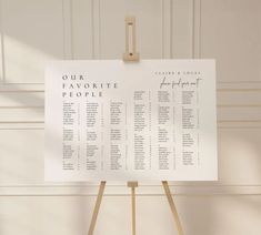 a table plan on a wooden easel in front of a white wall with the words our favorite people written on it