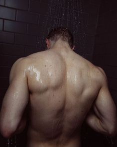 a man standing in the shower with his back turned to the camera and water coming out of his head