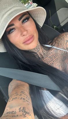 a woman with tattoos on her arm sitting in the back seat of a car wearing a hat