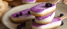 three purple desserts are stacked on top of each other with blueberries and cream