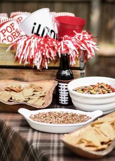 a table topped with bowls of food next to a bowl of chips and a football