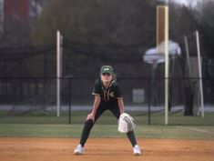 a woman in green and white uniform holding a catchers mitt on a baseball field