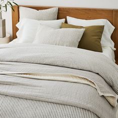 an unmade bed with white and grey striped sheets, pillows and blankets on it