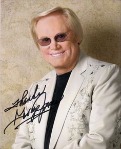 an older man in a white suit and sunglasses with his arms crossed, smiling at the camera