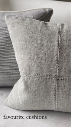 two gray pillows sitting on top of a white couch