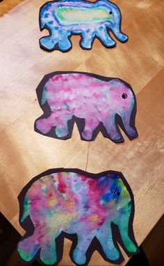 three elephants painted in different colors on a wooden table