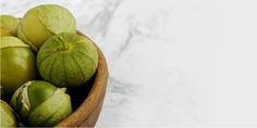 a wooden bowl filled with green fruit on top of a white countertop next to a marble wall