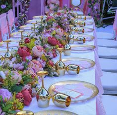 a long table is set with pink and gold place settings, flowers on the plates