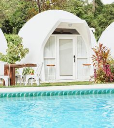 an outdoor swimming pool with chairs next to it and a white building in the background