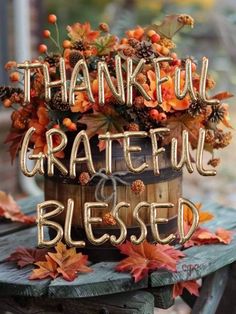 a wooden table topped with a bucket filled with fall leaves and words that say grateful