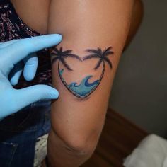 a woman's arm with two palm trees and a heart shaped tattoo on it