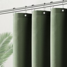 a green curtain hanging from a metal rod next to a window with a palm tree in the background