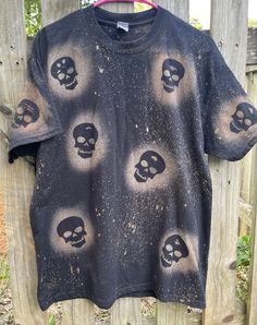 a t - shirt with skulls painted on it hanging from a wooden fence in the woods