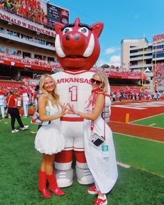 two women standing in front of a mascot at a football game