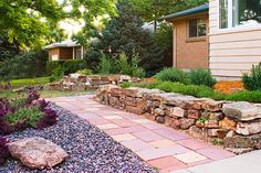 a stone wall in front of a house with purple flowers and rocks on the ground