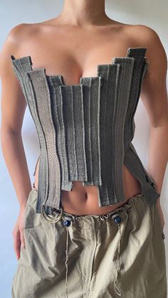 a woman wearing a gray corset with her hands on her hips, standing in front of a white wall