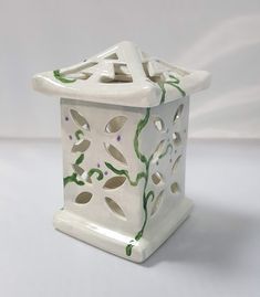 a white ceramic birdhouse with green leaves on it's sides and an open roof