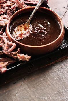 a wooden tray topped with lots of meat and dipping sauce on top of it's sides