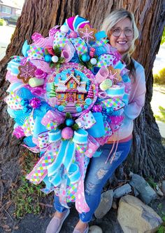 a woman is holding a large wreath in front of a tree with decorations on it