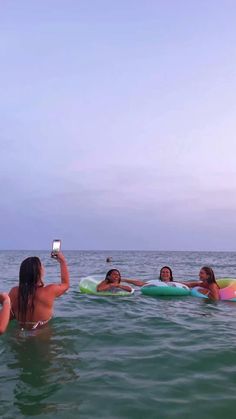 four people in the water taking pictures with their cell phones while floating on surfboards