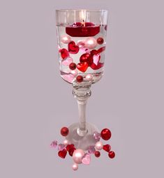 a wine glass filled with lots of pink and red heart shaped confetti next to a lit candle