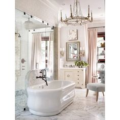 a large white bath tub sitting next to a walk in shower and a sink under a chandelier