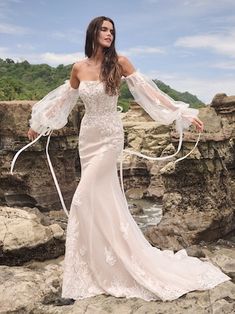 a woman in a wedding dress standing on rocks near the ocean with her arms outstretched