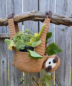 a stuffed animal hanging from a tree branch holding a potted plant in it's mouth