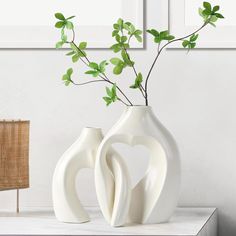 two white vases with green leaves in them