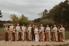 a group of people standing next to each other on top of a dirt field with trees in the background