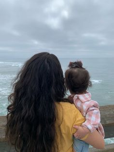 a woman holding a child looking out at the ocean