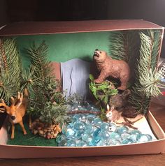 an open cardboard box with fake animals and plants in it on top of a wooden table