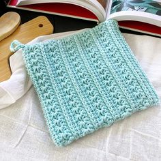 an open crochet book on a bed next to a wooden spoon